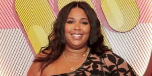 lizzo smiles at the camera, she wears a sheer black floral dress and gold necklaces