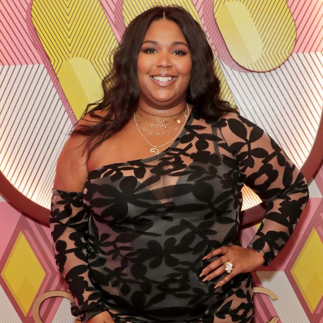 lizzo smiles at the camera, she wears a sheer black floral dress and gold necklaces