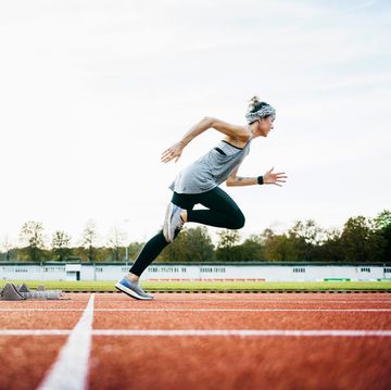 a woman wearing sports clothing sprinting off the starting blocks on an outdoor running track