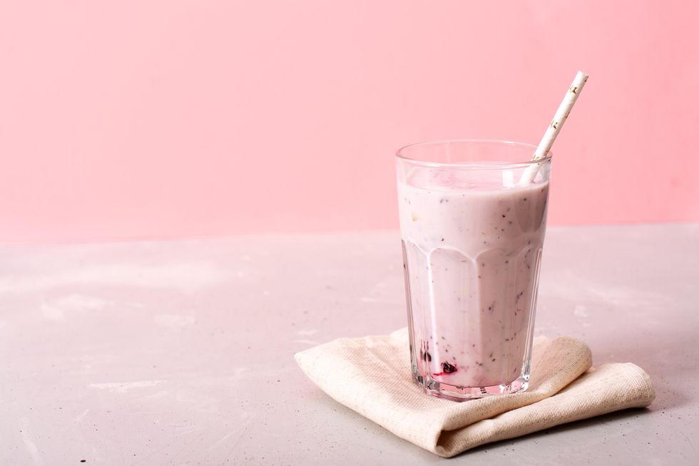 two glasses of blueberries smoothie on pink background poring from blender into glass