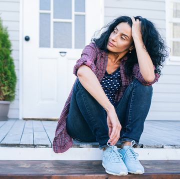 sad mid adult woman sitting on stairs in front of her house