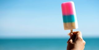 cropped image of womans hand holding ice cream by the sea against clear blue sky