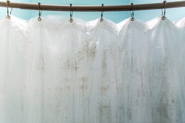 dark brown mildew mold on plastic interior shower curtain in a light aqua bathroom inside the bathtub and shower area