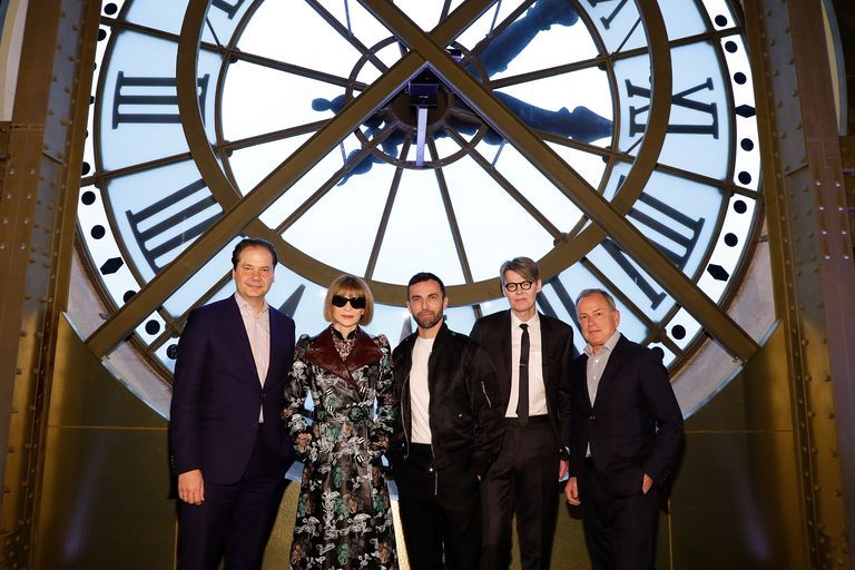 Max Hollein, Anna Wintour, Nicolas Ghesquiere, Andrew Bolton, and Michael Burke pose for a photo in front of a giant clock.