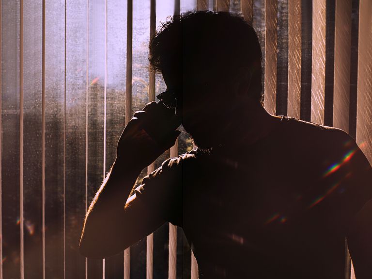 silhouette of an unknown man on a phone against window blinds conceptual with space for copy