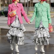 two women photographed on the street holding hands in pastel coats, silver dresses, and white boots
