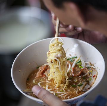thai Asian man eating Thai noodle soup from a bowl with wooden chopsticks.