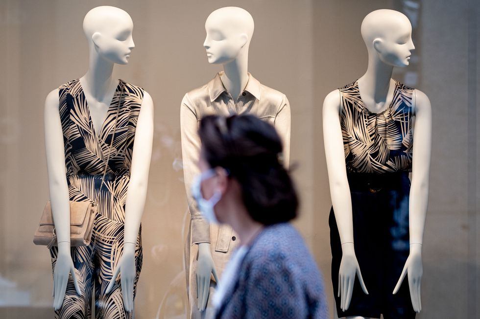 25 april 2020, lower saxony, hanover a woman wearing a mouthguard walks past the display of a fashion store, where three mannequins wearing dresses are on display photo peter steffendpa photo by peter steffenpicture alliance via getty images