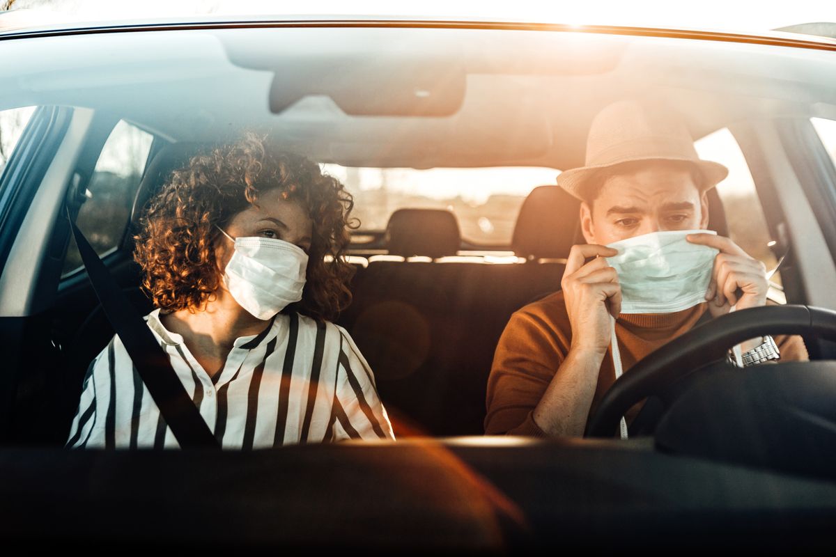 corona virus pandemic concept breathing through a medical mask because of the danger of getting the flu virus, influenza infection enjoying travel beautiful young couple sitting on the front passenger seats and smiling while handsome man driving a car
