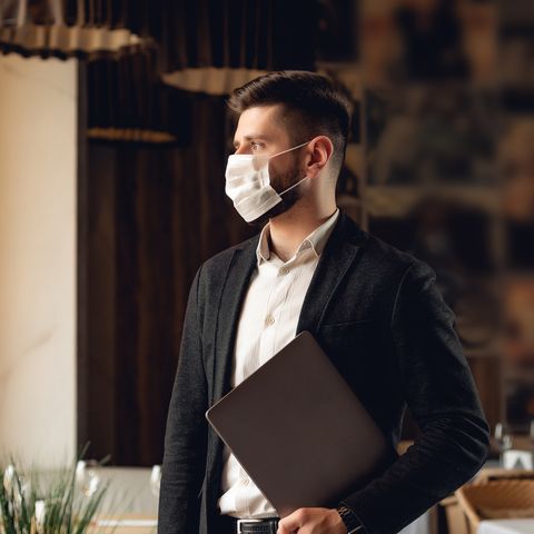 handsome adult bearded man indoors in cafe lifestyle concept photo with copy space picture with gray laptop and protective mask on the face