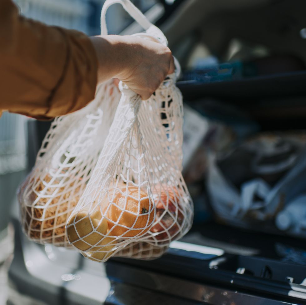 an asian chinese  female delivery person getting the groceries and fruit her customer order online shopping in recycle bags from her car trunk and deliver it to her customer