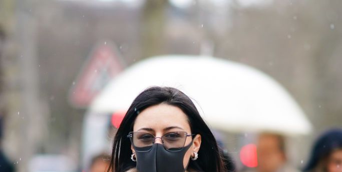 paris, france   february 29 a guest wears glasses, a brown wool pullover over the shoulders, a white long coat, a mesh black top, black bras, black pants, earrings, a protective face mask in a context of coronavirus covid 19 breakout, during paris fashion week   womenswear fallwinter 20202021, on february 29, 2020 in paris, france photo by edward berthelotgetty images