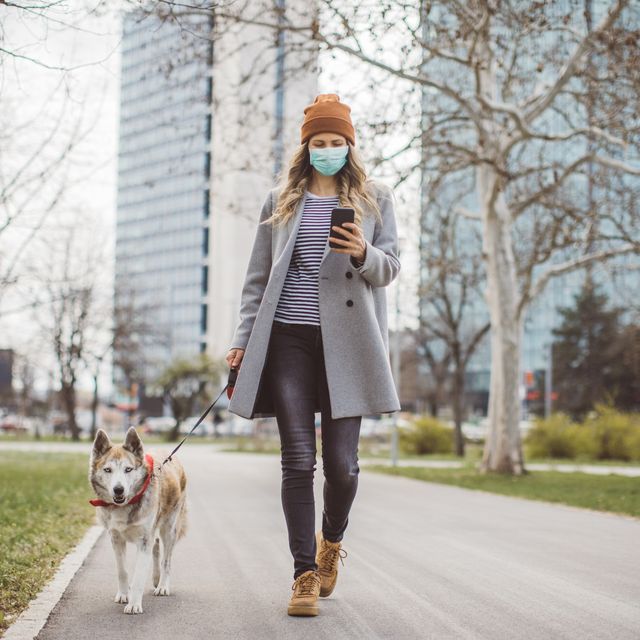 woman during pandemic isolation walking with her dog in park and use mobile phone