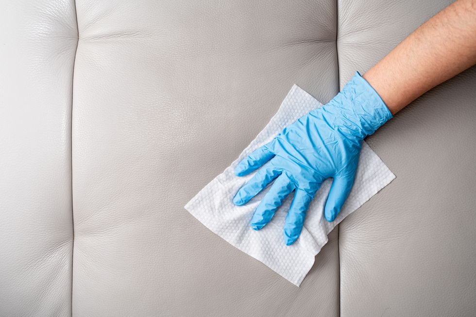 hands with blue protective glove wiping leather sofa with disinfection wipes directly above view