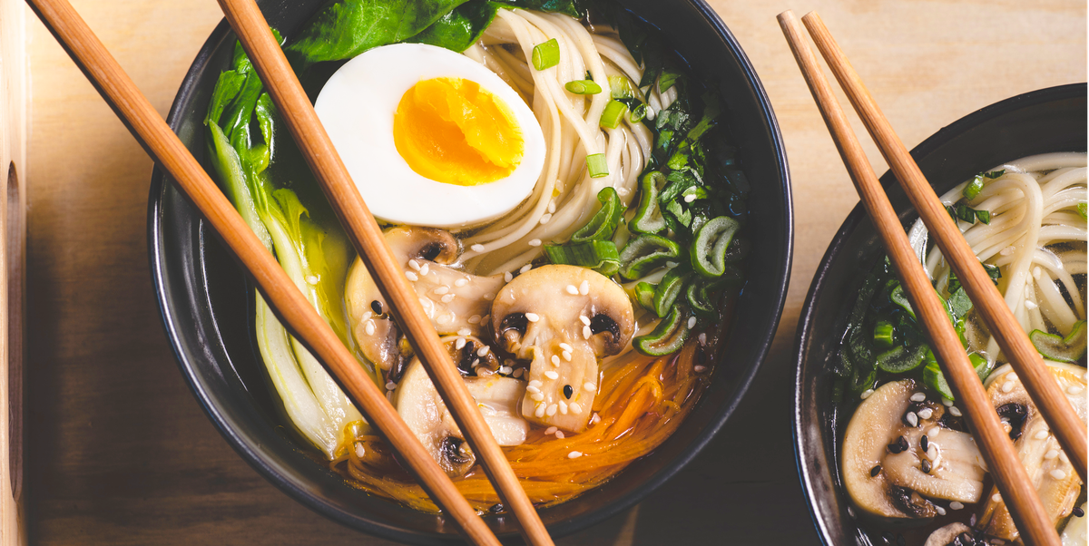 traditional japanese ramen soup with  mushrooms, bok choy, greens in  two black bowls on the orange background, top view, close up