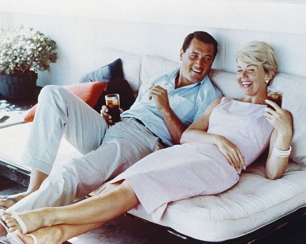 rock hudson 1925 1985, us actor, wearing white trousers and a light blue short sleeved shirt, and doris day, us singer and actress, in a pink gingham dress, both reclining on a sofa, laughing and holding drinks, circa 1960 photo by silver screen collectiongetty images