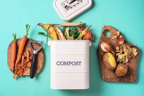 top view of kitchen food waste collected in recycling compost pot peeled vegetables on chopping board, white compost bin on blue background