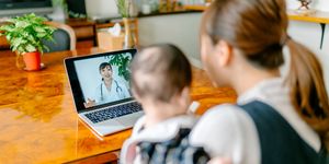 a mother with her baby is video calling a doctor on a laptop from home