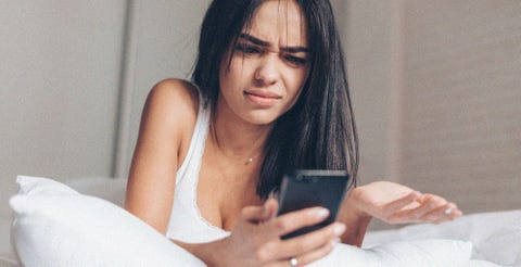 young annoyed angry woman looking on mobile phone in bed at home