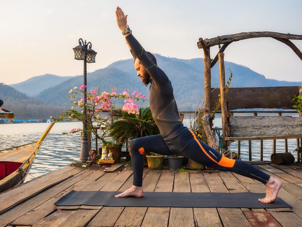 man doing a warrior pose during a yoga on wooden pier at mountain lake
