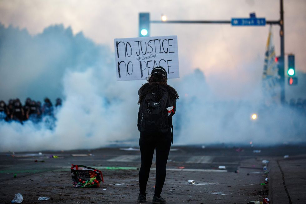 topshot   smoke rises near a demonstrator holding a sign and facing a row of police near the 5th police precinct during a demonstration to call for justice for george floyd, a black man who died while in custody of the minneapolis police, on may 30, 2020 in minneapolis, minnesota   clashes broke out and major cities imposed curfews as america began another night of unrest saturday with angry demonstrators ignoring warnings from president donald trump that his government would stop violent protests over police brutality cold photo by kerem yucel  afp photo by kerem yucelafp via getty images