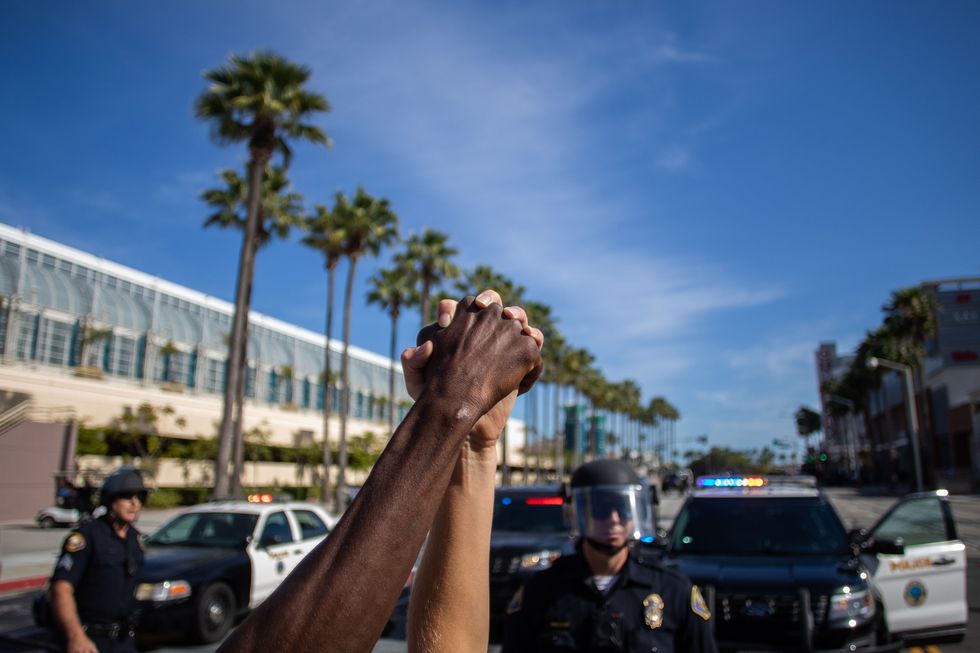 topshot   a black man and a white woman hold their hands up in a front of police officers in downtown long beach on may 31, 2020 during a protest against the death of george floyd, an unarmed black man who died while being arrested and pinned to the ground by the knee of a minneapolis police officer   protests sweeping the united states over the death of george floyd reverberated on the other side of the globe monday when thousands marched in solidarity on the streets of new zealand photo by apu gomes  afp photo by apu gomesafp via getty images