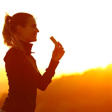 silhouette of runner woman eating energy bar after running at sunset in the mountain