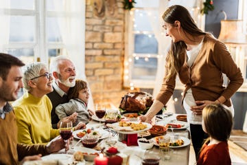 happy extended family enjoying while having thanksgiving meal at home young pregnant woman is serving food