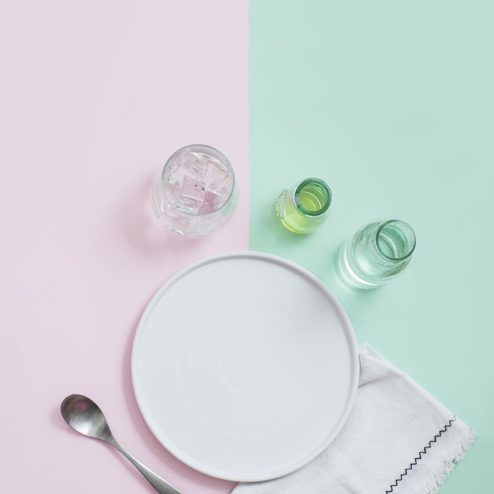 flat lay view of various white empty plates and other eating utensils on pastel coloured background