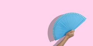 cropped woman hand holding a blue folding fan over pink background