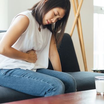young woman sitting on sofa in pain, clutching her stomach