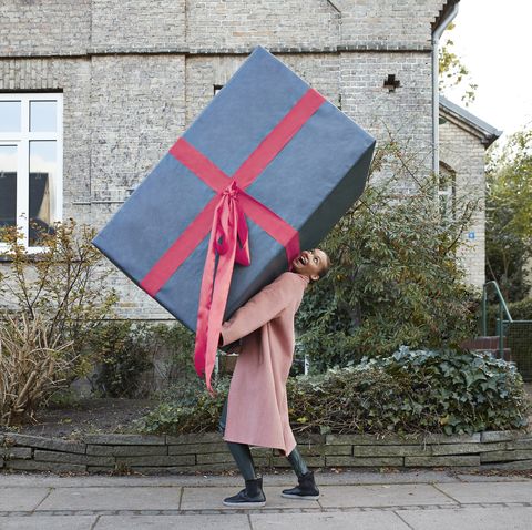 happy young woman carrying large gift box on footpath
