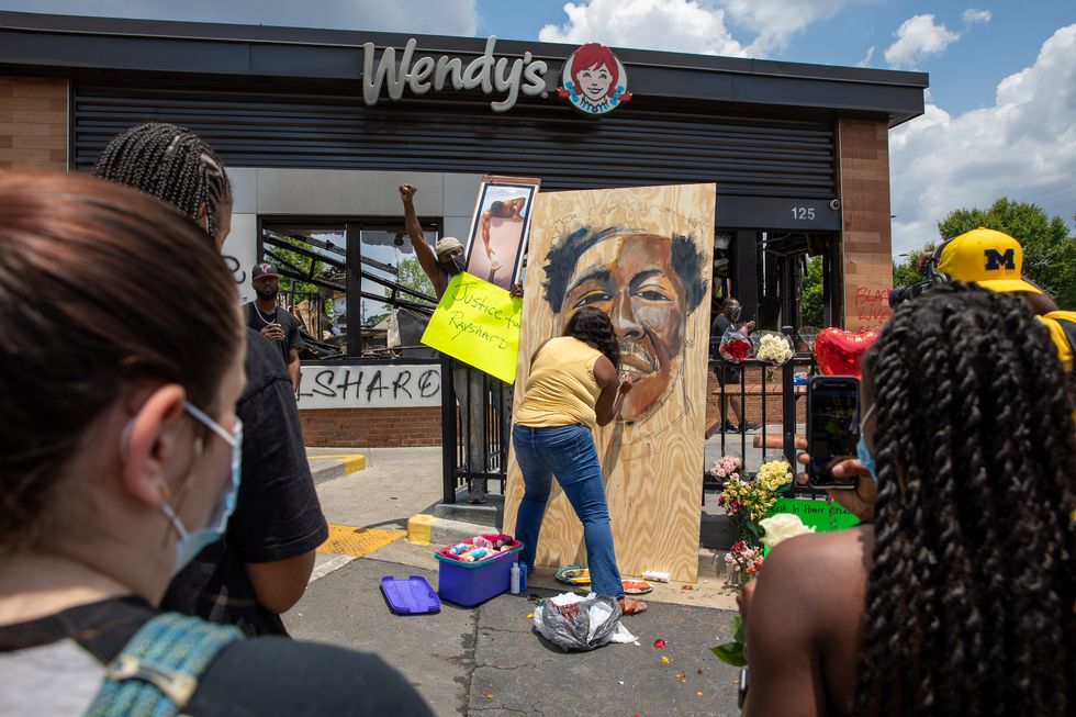 atlanta, ga   june 14 people gather at a memorial as a woman paints a portrait of rayshard brooks at the site of a wendy's restaurant set ablaze overnight on june 14, 2020 in atlanta, georgia brooks was shot and killed on june 12th by police in a struggle following a field sobriety test at the wendy's  photo by dustin chambersgetty images