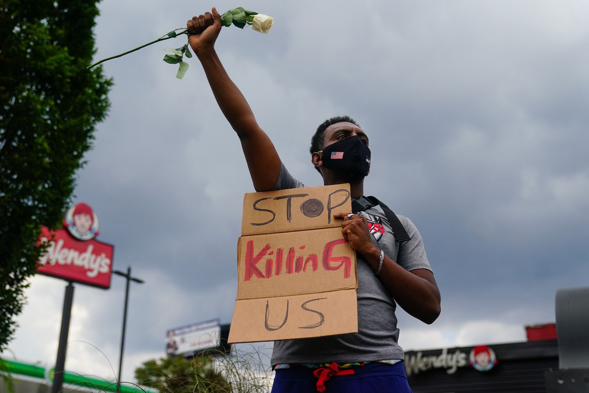 topshot   a man holds a sign and a white rose in his fist while facing traffic outside a burned wendys restaurant on the second day following the police shooting death of rayshard brooks in the restaurant parking lot june 14, 2020, in atlanta, georgia   the fatal shooting of a black man by a white police officer, this time in atlanta, georgia, poured more fuel june 14, 2020 on a raging us debate over racism after another round of street protests and the resignation of the city's police chief a wendy's restaurant where 27 year old rayshard brooks was killed was set on fire june 13, 2020 and hundreds of people marched to protest the killing photo by elijah nouvelage  afp photo by elijah nouvelageafp via getty images