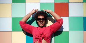 young woman in stylish casuals and sunglasses looking excited against multicolored tiled wall african american female looking at camera and smiling