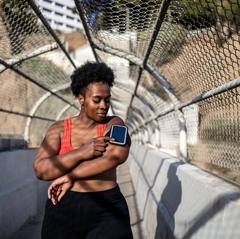 healthy woman touching phone screen on armband before exercising outdoors african american woman in sports clothing using phone while exercising outdoors