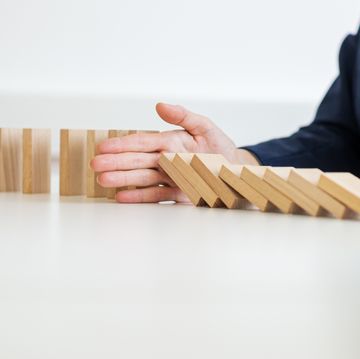 wide view image of unrecognizable business woman sitting at her white office desk stopping collapsing dominos with her hand in a conceptual image of crisis management