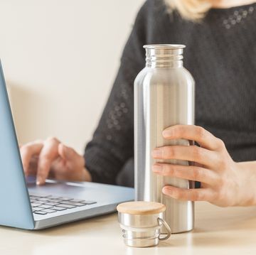 white woman holding her personal stainless steel water bottle on the working table daily hydration habit to stay healthy