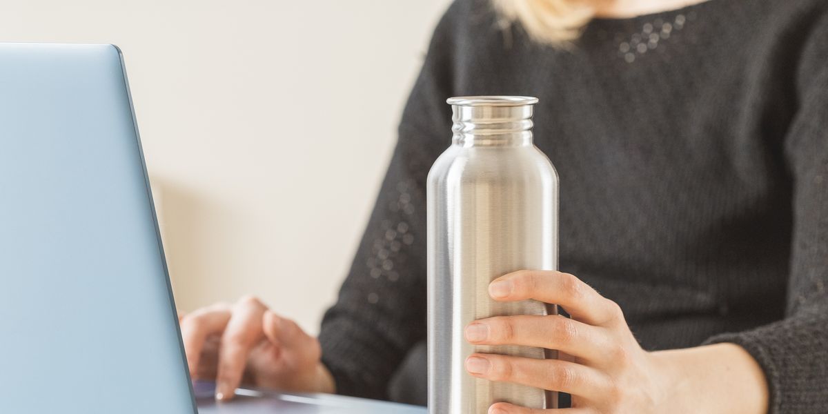 white woman holding her personal stainless steel water bottle on the working table daily hydration habit to stay healthy