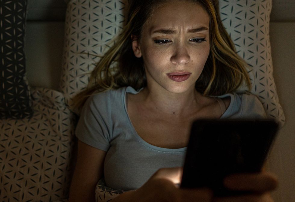 young woman is lying in the bed and looking confused at smart phone