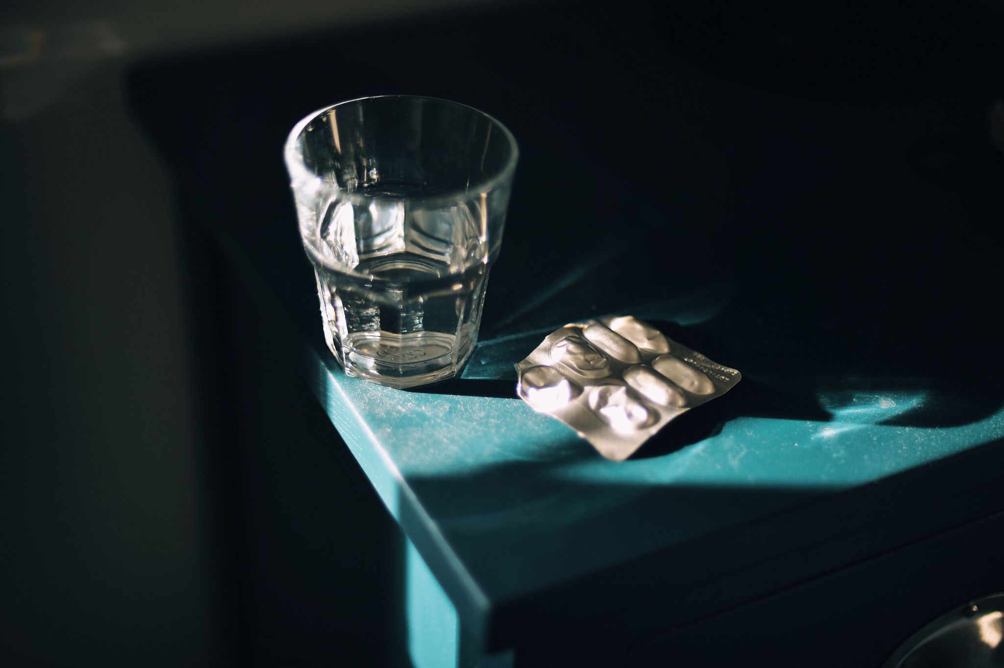 glass of water in strong sunlight on blue bedside table with blister pack of medication pills