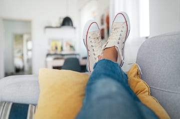 young female lying in new beige sneaker son cozy comfortable living room sofa putting feet on pillows and resting and relaxing. comfortable clothing and footwear concept