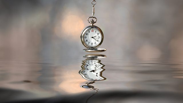 pocket watch hanging above water with a reflective surface