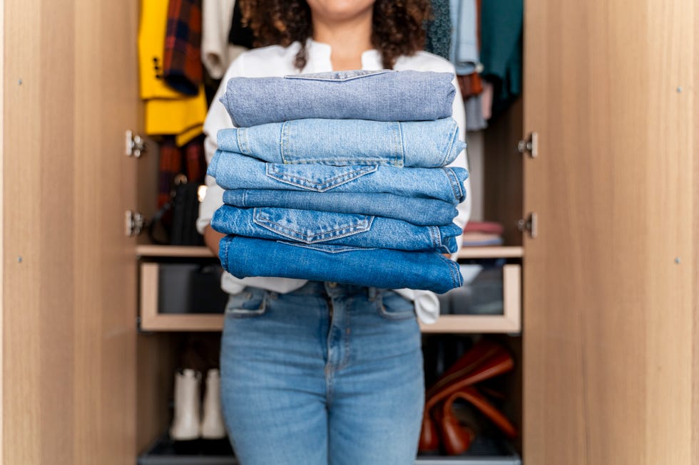 woman standing on front of wardrobe holding stack of blue jeans