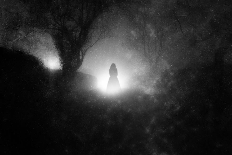 A country lane, on a foggy night with a ghostly woman in a dress. in front of glowing lights. With a grunge, blurred, vintage edit a country lane, on a foggy night with a ghostly woman in a dress in front of glowing lights with a grunge, blurred, vintage edit