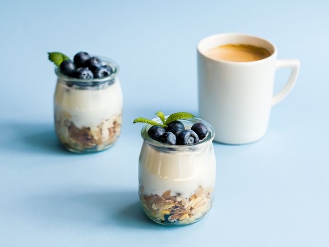 homemade natural yogurt with granola and blueberries in glass jars and coffee on blue background healthy breakfast set