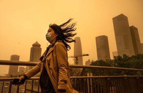 tijdens een seizoensgebonden zandstorm in beijing china trotseert een vrouw de harde wind wetenschappers denken dat de frequentie en intensiteit van dit soort zandstormen toenemen als gevolg van woestijnvorming en de opwarming van de aarde door de co2uitstoot als gevolg van het verbruik van fossiele brandstoffen en de daaruit voortkomende klimaatverandering lijdt china ook onder zware luchtvervuiling
