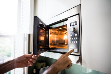 a man using a microwave oven his finger on the opening button