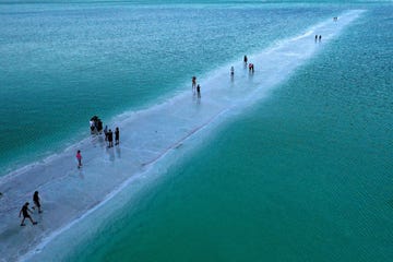 a picture taken on september 22, 2021, shows people walking on dirt of salt between evaporation ponds in the southern part of the dead sea, where both sodium chloride and potassium salts are produced by dead sea works factories, near the israeli neve zohar resort a spectacular expanse of water in the desert, flanked by cliffs to east and west, the dead sea has lost a third of its surface area since 1960 the blue water recedes about a metre yard every year, leaving behind a lunar landscape whitened by salt and perforated with gaping holes photo by menahem kahana afp photo by menahem kahanaafp via getty images