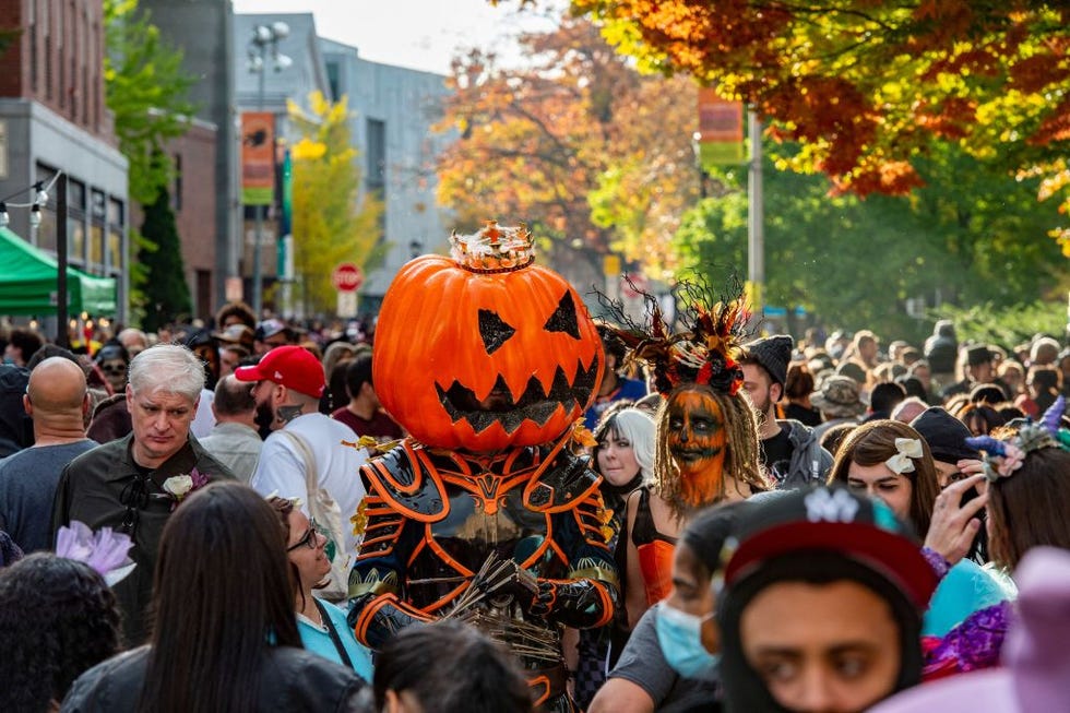 a large pumpkin headed costumed reveller walks with others through a crowded street on halloween in salem, massachusetts